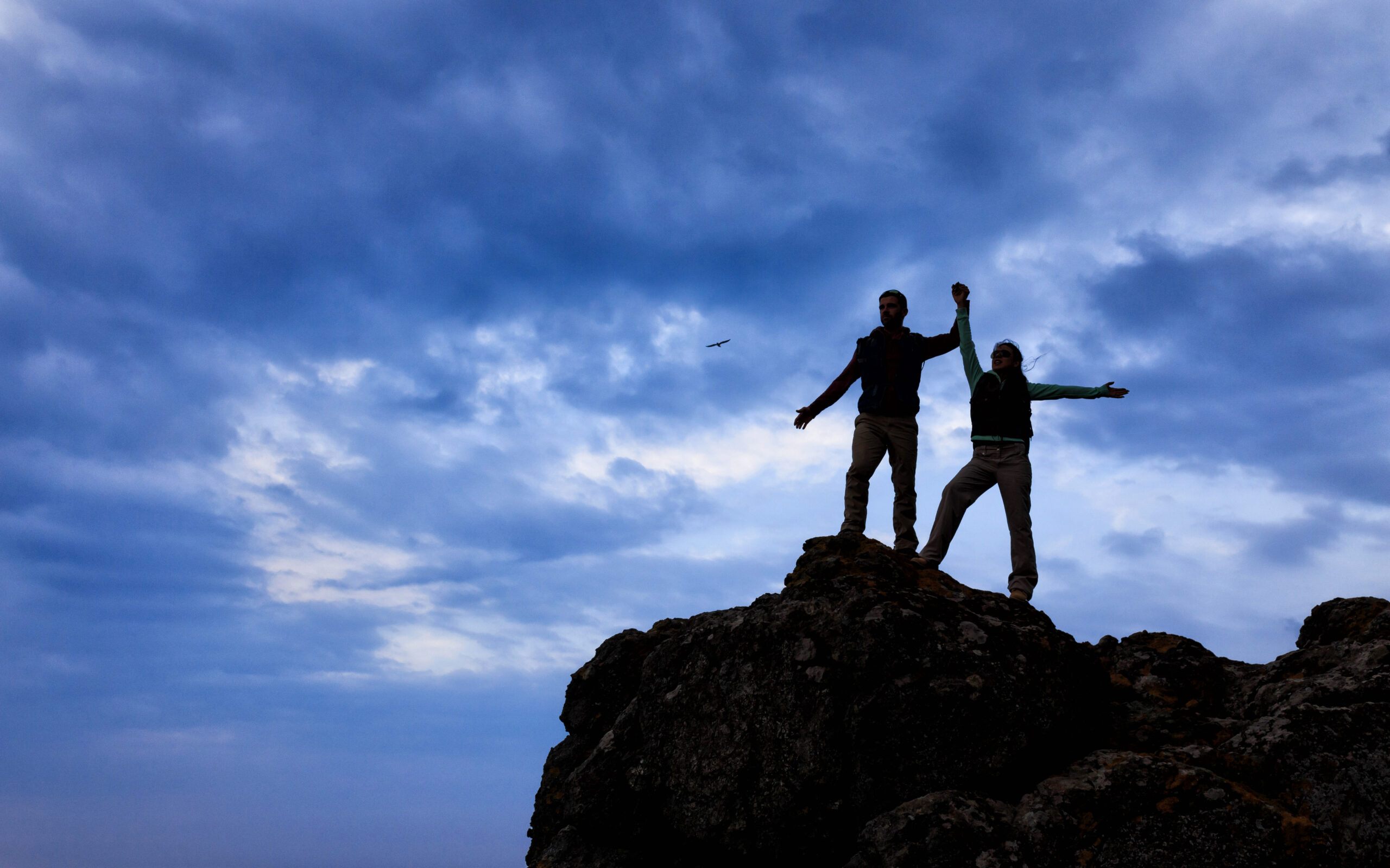 Silhouettes of backpackers standing on top of mountain